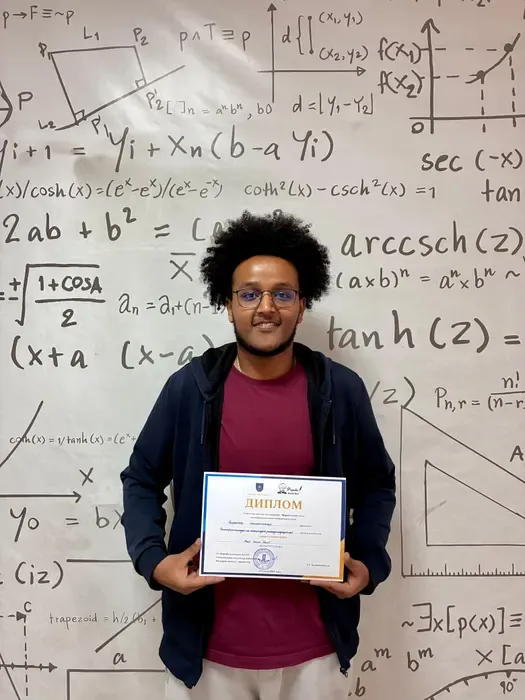 Samson holding his conference certificate in front of a board of equations.